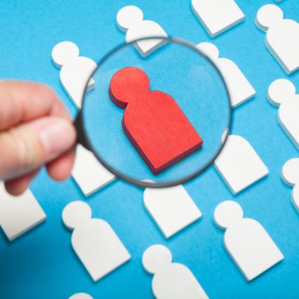 Magnifying glass highlighting standout red figure among white figures.