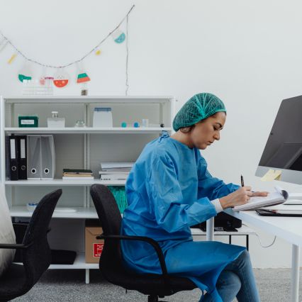 Laboratory worker in blue scrubs writing at a desk.